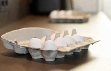 Mutfak masasındaki karton kutuda, arka planda bulanık bir düzine beyaz yumurtayı kapat. 