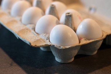 Mutfak masasındaki karton kutuda, arka planda bulanık bir düzine beyaz yumurtayı kapat. 