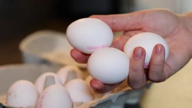 Beyaz yumurta tutan, arka planda bulanık arka planda gri mutfak masasındaki karton kutuda bir düzine yumurta tutan bir kadının fotoğrafını çek.