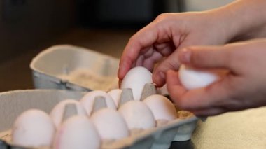Mutfak masasındaki karton bir kutudan arka planda bulanık olan beyaz yumurtaları alan kadın ellerini kapatın. Yüksek kaliteli FullHD görüntüler