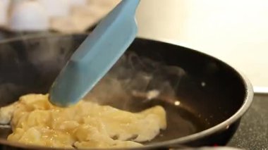 Omlet yumurtalarını siyah bir tavada yapmaya yakın, arka planda beyaz yumurtalarla bulanık mutfak masası. Yüksek kaliteli FullHD görüntüler