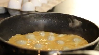 Omlet yumurtalarını siyah bir tavada yapmaya yakın, arka planda beyaz yumurtalarla bulanık mutfak masası. Yüksek kaliteli FullHD görüntüler