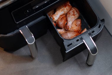 İçinde çiğ ve baharatlı tavuk budu olan açık siyah bir hava kızartma makinesini kapat. Yağsız sağlıklı yemek.