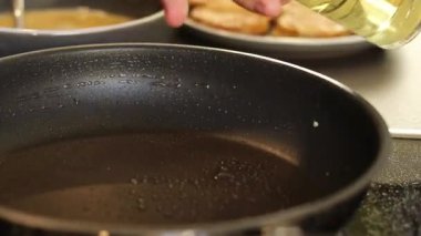 Mutfak arka planında bulanık, siyah bir tavaya yağ püskürten bir kadının fotoğrafını çek. Ev konseptinde sağlıklı yemek pişirme. Yüksek kaliteli FullHD görüntüler