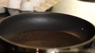 Omlet yumurtalarını siyah bir tavada yapmaya yakın, arka planda beyaz yumurtalarla bulanık mutfak masası. Yüksek kaliteli FullHD görüntüler