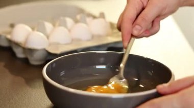 Gri bir kasede çatalla yumurta çırpan, arka planı bulanık ve karton bir kutuda beyaz yumurtaları olan kadınların ellerini kapatın. Yüksek kaliteli FullHD görüntüler