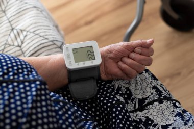 Evde modern dijital tonometre cihazıyla kan basıncını ölçen yaşlı bir kadına yakın çekim.