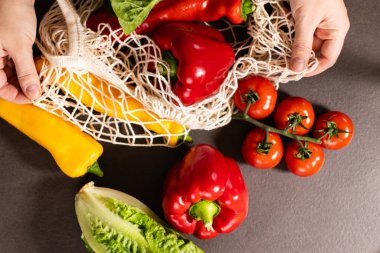 Gri mutfak masasındaki alışveriş çantasından taze mevsimlik sebzeleri çıkaran kadın ellerinin en üst görüntüsü. Sıfır atık ve çevre dostu market alışveriş konsepti 