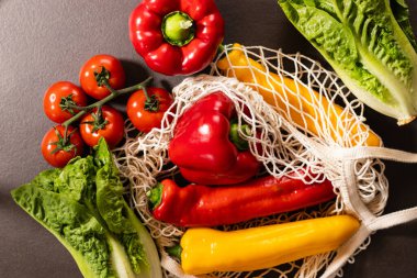 Gri mutfak masasındaki eko ağ alışveriş çantasında taze mevsimlik sebzelerin en üst görüntüsü. Sıfır atık ve çevre dostu market alışveriş konsepti 