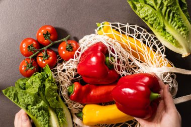 Gri mutfak masasındaki alışveriş çantasından taze mevsimlik sebzeleri çıkaran kadın ellerinin en üst görüntüsü. Sıfır atık ve çevre dostu market alışveriş konsepti 