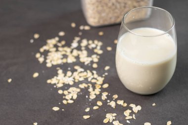 Bir bardak laktozsuz yulaf ezmesi ve yulaf ezmesi gri mutfak masasında, arka planda bulanık. Vejetaryen ve sütsüz alternatif süt kavramı