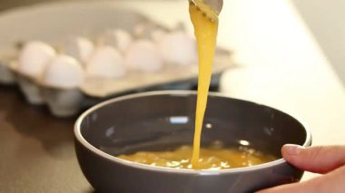 Gri bir kasede çatalla yumurta çırpan, arka planı bulanık ve karton bir kutuda beyaz yumurtaları olan kadınların ellerini kapatın. Yüksek kaliteli FullHD görüntüler