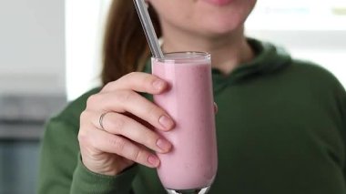 Kafkasyalı bir kadının metal kamışlı, bulanık mutfak arka planlı bir bardaktan çilekli smoothie içerkenki görüntüsü. Yüksek kaliteli FullHD görüntüler