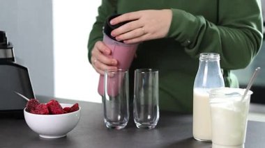 Mutfakta yoğurt ve sütle taze çilekli smoothie hazırlayan yeşil kazaklı bir kadının fotoğrafını çek. Yüksek kaliteli FullHD görüntüler
