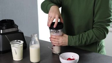 Mutfakta yoğurt ve sütle taze çilekli smoothie hazırlayan yeşil kazaklı bir kadının fotoğrafını çek. Yüksek kaliteli FullHD görüntüler