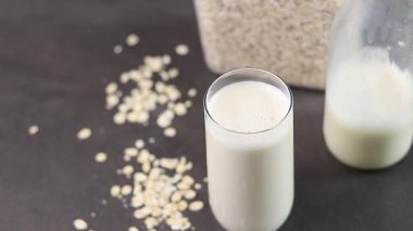 Gri mutfak masasındaki plastik kutuda bir bardak yulaf sütü ve yulaf ezmesi. Vejetaryen ve sütsüz alternatif süt konsepti. Yüksek kaliteli FullHD görüntüler