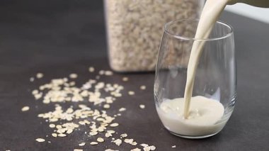 Gri mutfak masasındaki bir bardağa yulaf sütü döken bir kadının elini kapat. Vejetaryen ve sütsüz alternatif süt konsepti. Yüksek kaliteli FullHD görüntüler