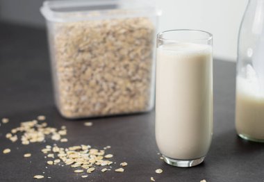 Bir bardak laktozsuz yulaf ezmesi ve yulaf ezmesi gri mutfak masasında, arka planda bulanık. Vejetaryen ve sütsüz alternatif süt kavramı