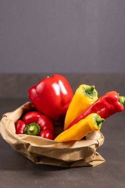 Kırmızı dolmalık biberi kapat ve koyu gri mutfak masasındaki eko kağıt torbada kırmızı biber koy.