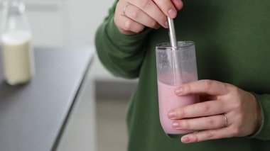 Kafkasyalı bir kadının metal kamışlı, bulanık mutfak arka planlı bir bardaktan çilekli smoothie içerkenki görüntüsü. Yüksek kaliteli FullHD görüntüler