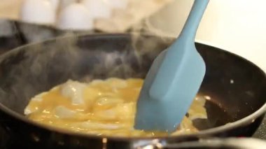 Omlet yumurtalarını siyah bir tavada yapmaya yakın, arka planda beyaz yumurtalarla bulanık mutfak masası. Yüksek kaliteli FullHD görüntüler