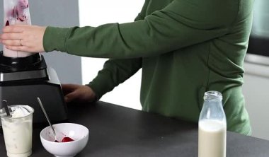 Mutfakta yoğurt ve sütle taze çilekli smoothie hazırlayan yeşil kazaklı bir kadının fotoğrafını çek. Yüksek kaliteli FullHD görüntüler