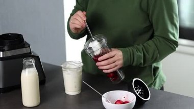 Mutfakta yoğurt ve sütle taze çilekli smoothie hazırlayan yeşil kazaklı bir kadının fotoğrafını çek. Yüksek kaliteli FullHD görüntüler