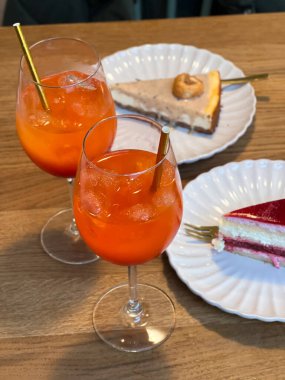 İki portakallı kokteyl ve beyaz tabakta iki dilim kek, ahşap kafe masası.