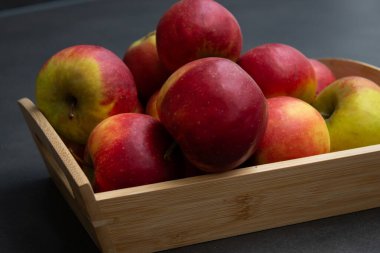 Koyu gri masa arkaplanındaki ahşap sandıkta taze, küçük organik kırmızı elmalar.