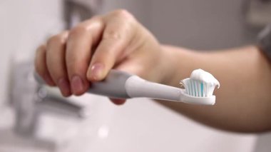 Elinde elektrikli, modern bir diş fırçası olan, bulanık bir banyo arkaplanı olan bir kadının yakın çekimi. Yüksek kaliteli FullHD görüntüler