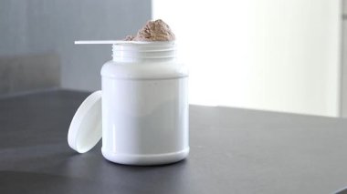 Mutfakta protein içeceği hazırlayan kadına yakın çekim. Kilo vermenin yerine diyet yemeği. Masada beyaz beyaz protein tozu kutusu var. Yüksek kaliteli FullHD görüntüler