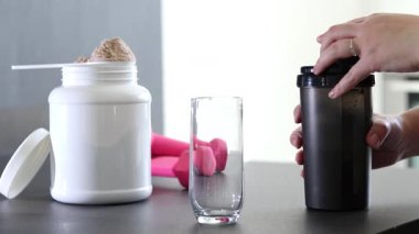 Kadının bardağa protein içeceği döktüğü yakın plan. Kilo vermenin yerine diyet yemeği. Beyaz beyaz protein tozu kutusu. Yüksek kaliteli FullHD görüntüler