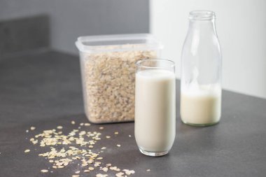 Bir bardak laktozsuz yulaf ezmesi ve yulaf ezmesi gri mutfak masasında, arka planda bulanık. Süt konsepti için vegan ve süt ürünleri alternatifi