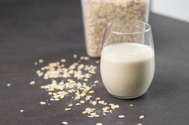 Bir bardak laktozsuz yulaf ezmesi ve yulaf ezmesi gri mutfak masasında, arka planda bulanık. Vejetaryen ve sütsüz alternatif süt kavramı