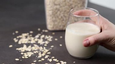 Gri mutfak masasındaki plastik kutuda bir bardak yulaf sütü ve yulaf ezmesi. Vejetaryen ve sütsüz alternatif süt konsepti. Yüksek kaliteli FullHD görüntüler