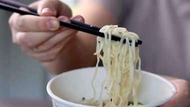 Yemek çubuklarıyla ramen yiyen bir dişinin fincanından plastik yemek. Asya fast-food 'u evde. Yüksek kaliteli FullHD görüntüler