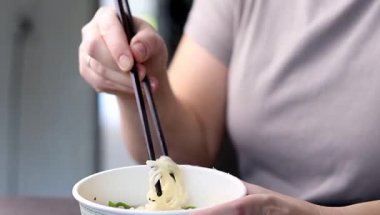 Yemek çubuklarıyla ramen yiyen bir dişinin fincanından plastik yemek. Asya fast-food 'u evde. Yüksek kaliteli FullHD görüntüler