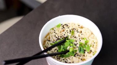 Basit ramen şehriyelerini plastik bir fincanda yemek çubuklarıyla kapatıyoruz. Gri masa arkaplanı. Asya fast-food konsepti. Yüksek kaliteli FullHD görüntüler