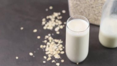 Gri mutfak masasındaki plastik kutuda bir bardak yulaf sütü ve yulaf ezmesi. Vejetaryen ve sütsüz alternatif süt konsepti. Yüksek kaliteli FullHD görüntüler