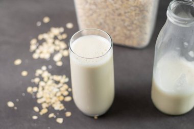 Bir bardak laktozsuz yulaf ezmesi ve yulaf ezmesi gri mutfak masasında, arka planda bulanık. Vejetaryen ve sütsüz alternatif süt kavramı