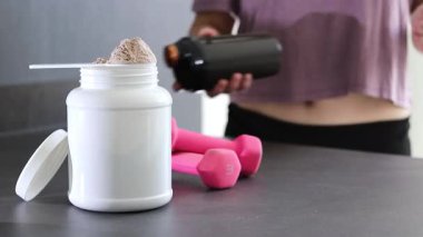 Protein tozu kutusunu ve masadaki pembe dambılları kapatın. Kadın protein içeceği hazırlıyor. Kilo vermenin yerine diyet yemeği. - Evet. Yüksek kaliteli FullHD görüntüler
