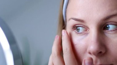 Gözlerinin altındaki yeşil jel nemlendirici bantlar kullanarak makyajsız, bin yıllık beyaz bir kadının fotoğrafını çek. Evde doğal cilt bakım rutini. Yüksek kaliteli FullHD görüntüler