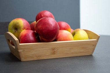 Koyu gri masa arkaplanındaki ahşap sandıkta taze, küçük organik kırmızı elmalar.