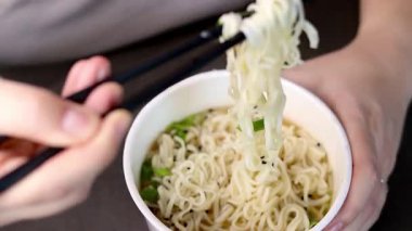 Yemek çubuklarıyla ramen yiyen bir dişinin fincanından plastik yemek. Asya fast-food 'u evde. Yüksek kaliteli FullHD görüntüler