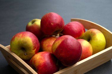 Koyu gri masa arkaplanındaki ahşap sandıkta taze, küçük organik kırmızı elmalar.