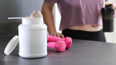 Protein tozu kutusunu ve masadaki pembe dambılları kapatın. Kadın protein içeceği hazırlıyor. Kilo vermenin yerine diyet yemeği. - Evet. Yüksek kaliteli FullHD görüntüler