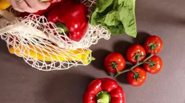 Gri mutfak masasındaki alışveriş çantasından taze mevsimlik sebzeleri çıkaran kadın ellerinin en üst görüntüsü. Sıfır atık ve çevre dostu market alışveriş konsepti. Yüksek kaliteli FullHD görüntüler