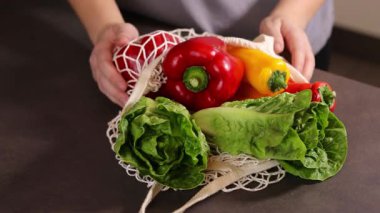 Gri mutfak masasındaki alışveriş çantasından taze mevsimlik sebzeleri çıkaran kadın ellerini kapat. Sıfır atık ve çevre dostu market alışveriş konsepti. Yüksek kaliteli FullHD görüntüler