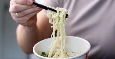 Yemek çubuklarıyla ramen yiyen bir dişinin fincanından plastik yemek. Asya fast-food 'u evde. Yüksek kaliteli FullHD görüntüler