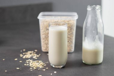 Bir bardak laktozsuz yulaf ezmesi ve yulaf ezmesi gri mutfak masasında, arka planda bulanık. Vejetaryen ve sütsüz alternatif süt kavramı